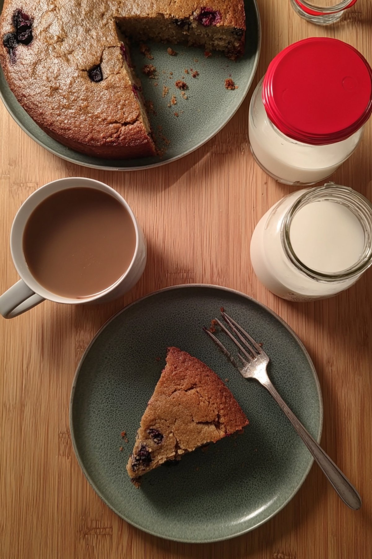 Part de gâteau petit déjeuner servie dans une assiette avec une tasse de café et des bouteilles de lait en arrière-plan.