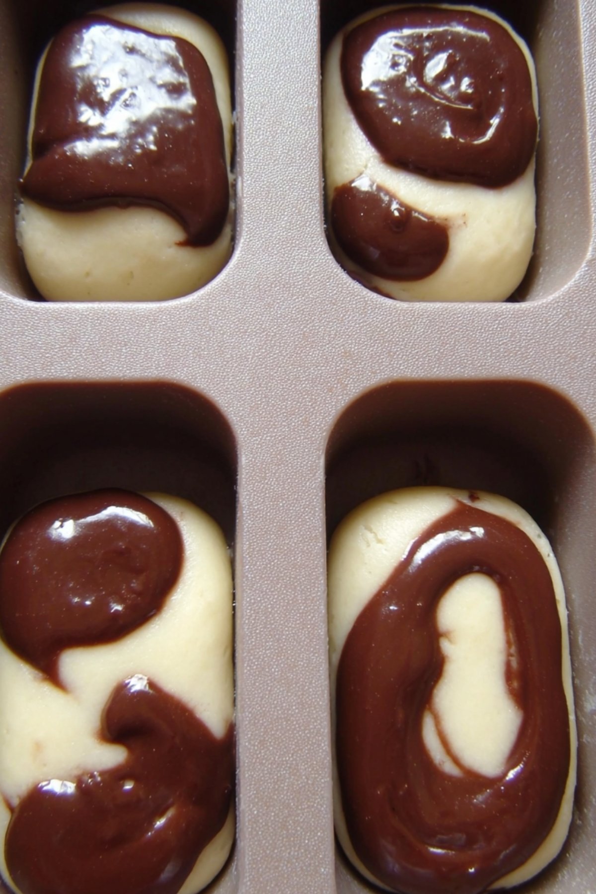 Empreintes de moule remplies de pâte vanille avec ajouts de pâte cacao au centre, étape pour marbrer un petit gateau.