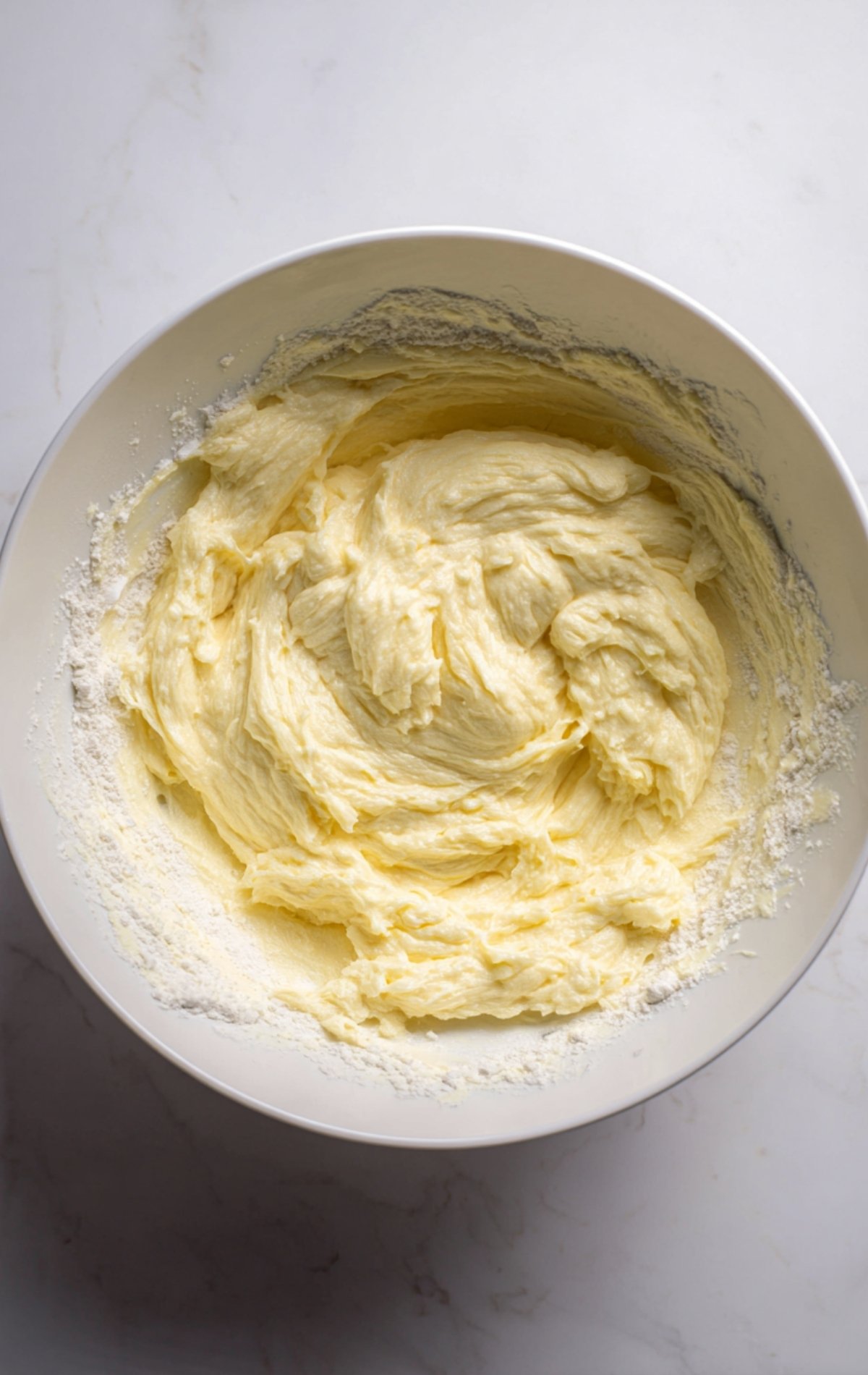 Pâte à gâteau jaune pâle, lisse et épaisse dans un grand saladier blanc.