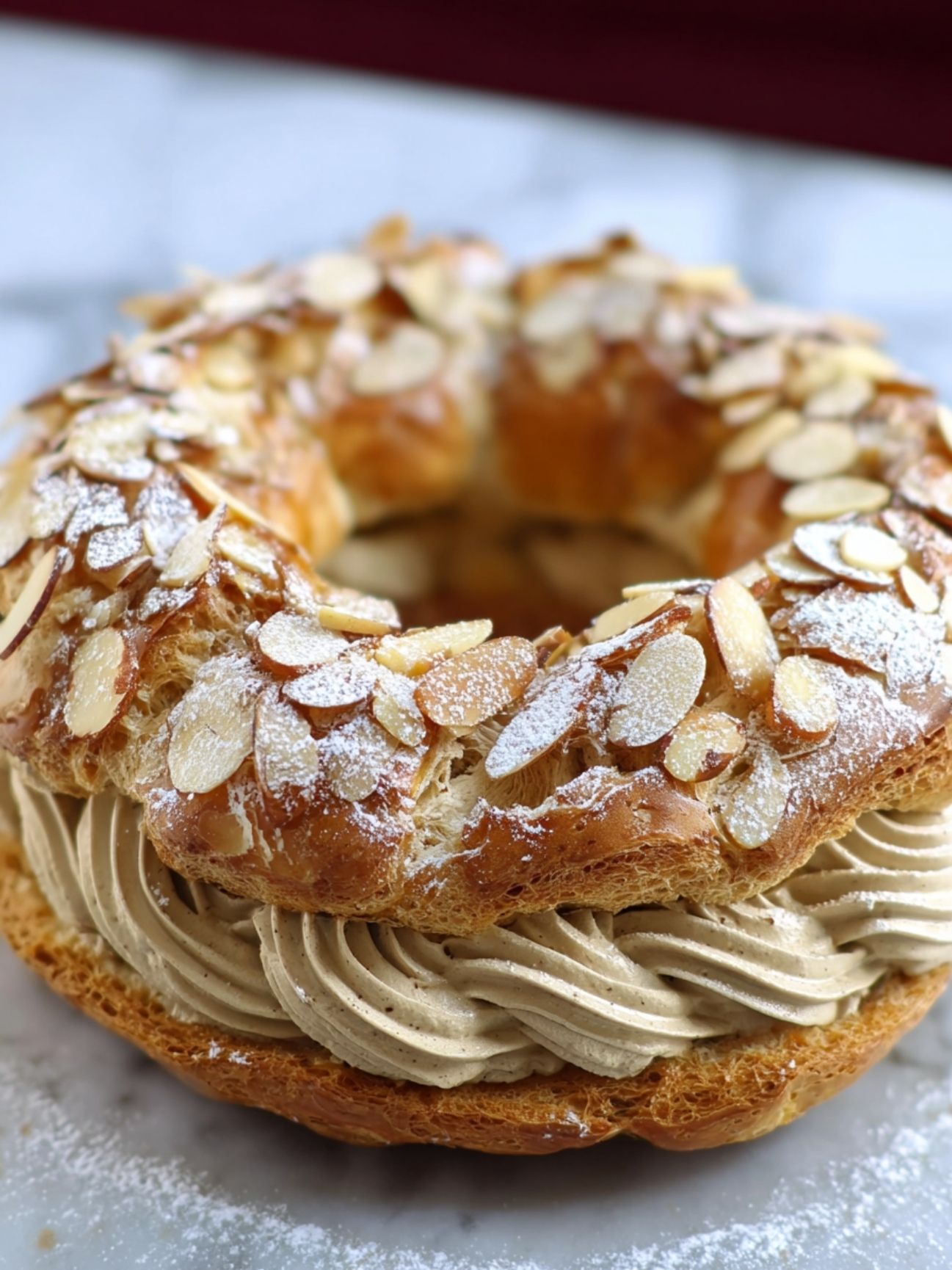 Gros plan sur un Paris-Brest maison garni d'amandes effilées et de crème onctueuse.