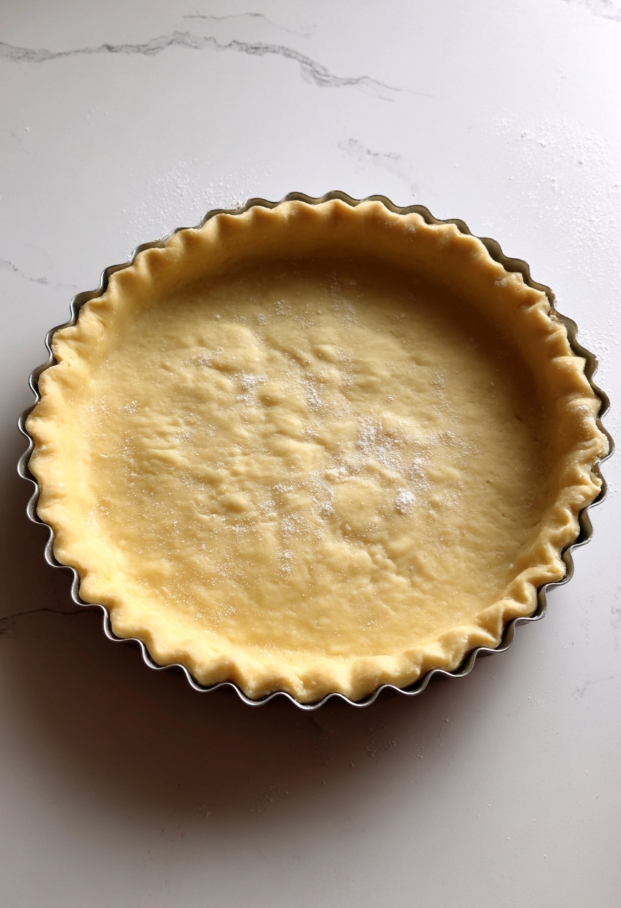 Fond de tarte piqué à la fourchette dans un moule cannelé avant d'ajouter la garniture aux prunes