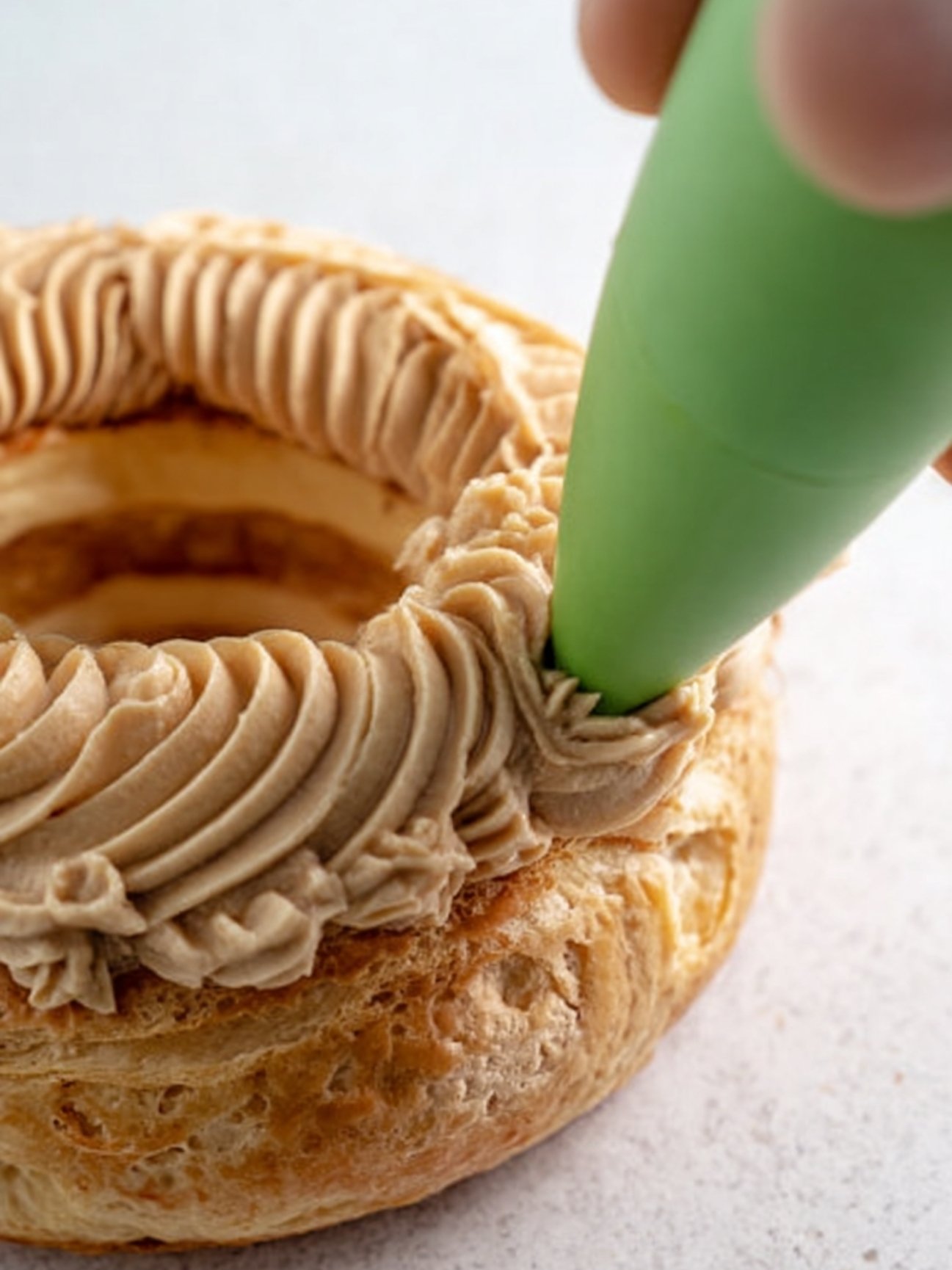 Pochage de la crème pralinée sur la base d'une couronne en pâte à choux.
