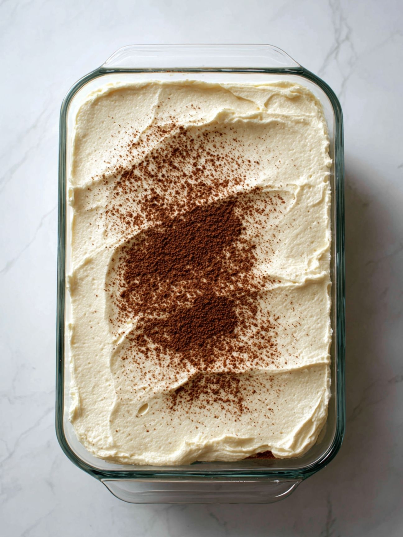 Tiramisu sans oeuf terminé dans un plat en verre avec un saupoudrage généreux de cacao amer.