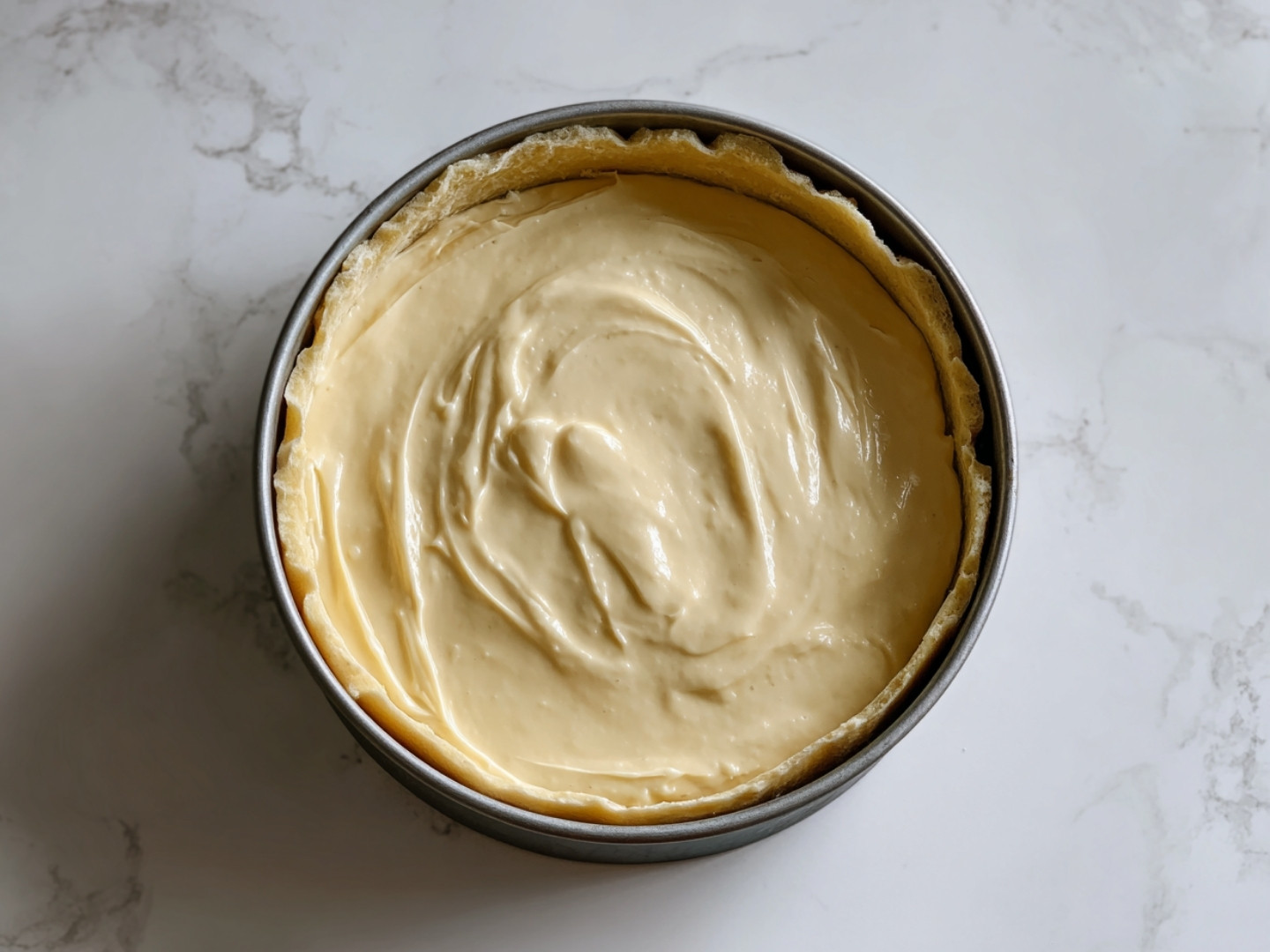 Appareil à flan vanillé versé sur une pâte brisée dans un moule avant la cuisson au four.