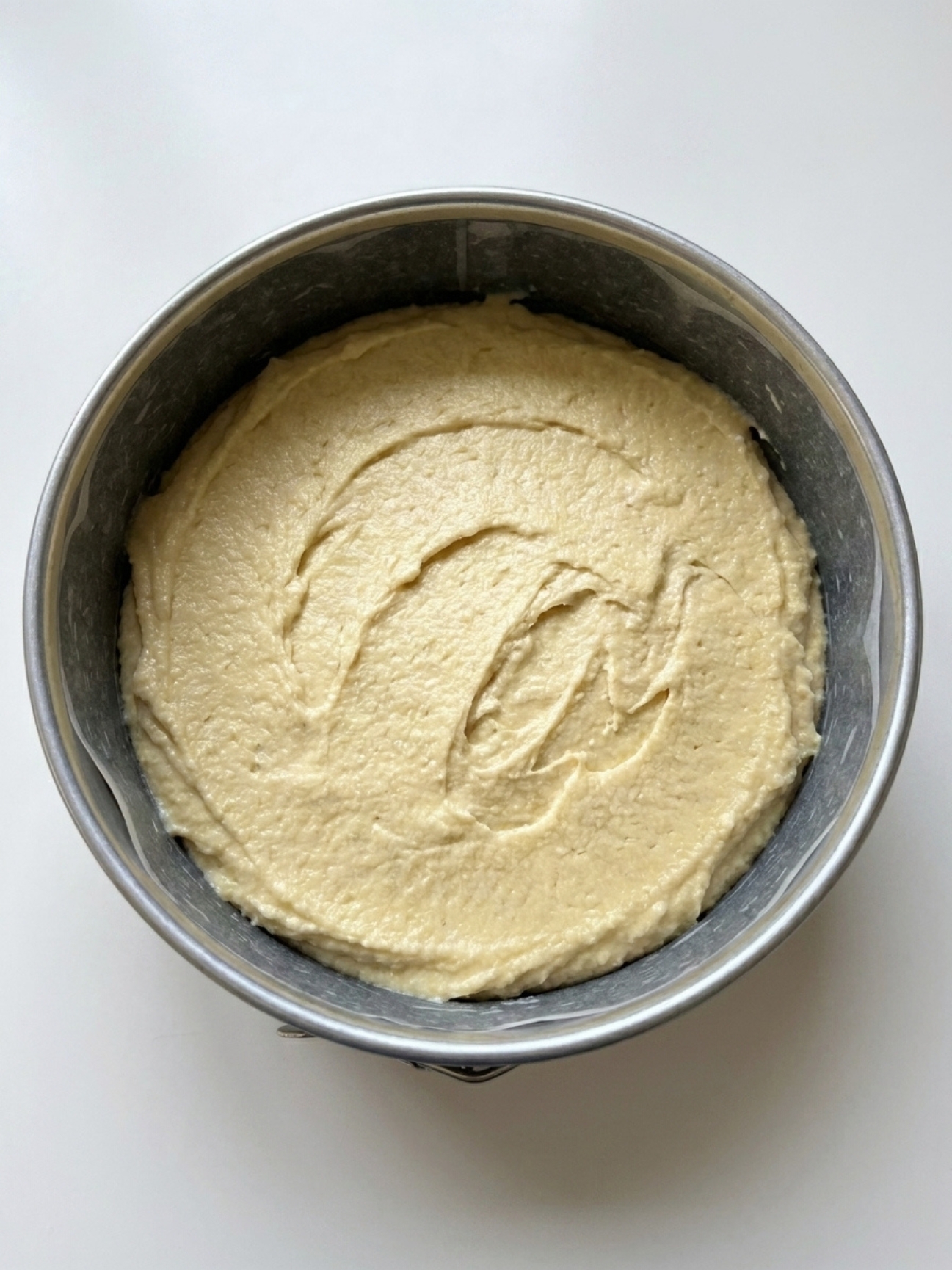 Pâte à gâteau nuage mascarpone étalée uniformément dans un moule à charnière prêt pour la cuisson.