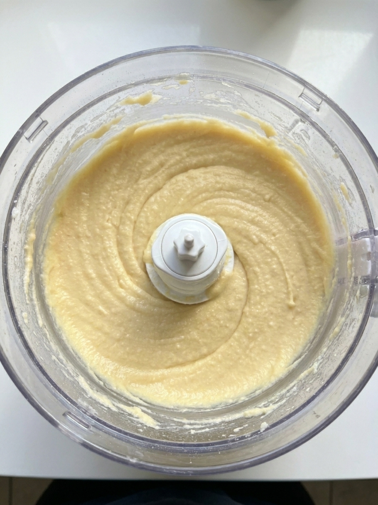 Pâte lisse jaune claire pour gâteau nuage mascarpone en train d'être mélangée dans un robot culinaire.