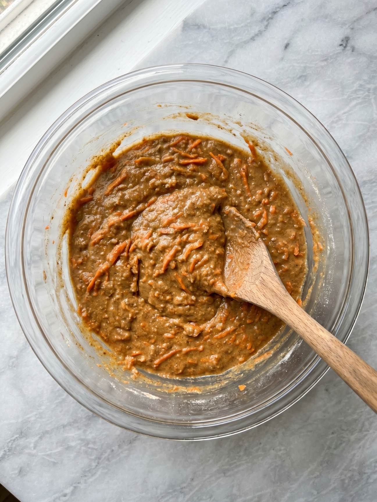 Main mélangeant une pâte avec des carottes râpées dans un bol pour gateau carotte pour chien.