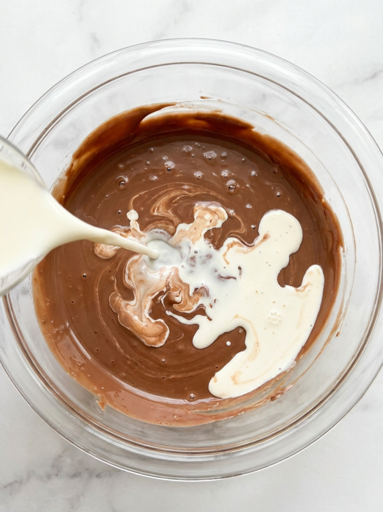 De la crème liquide blanche versée dans un bol de chocolat au lait fondu brillant.
