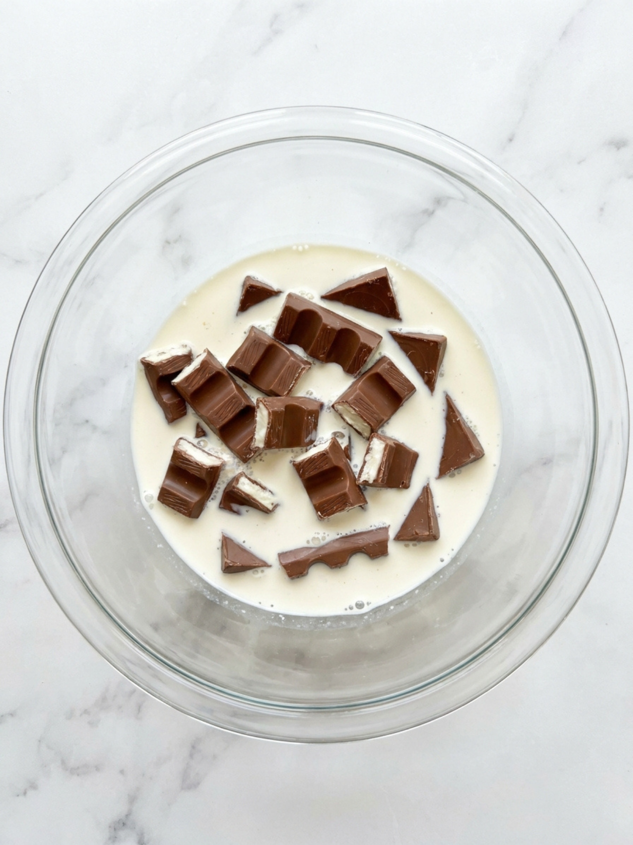 Morceaux de barres chocolatées Kinder Maxi immergés dans de la crème blanche dans un bol transparent