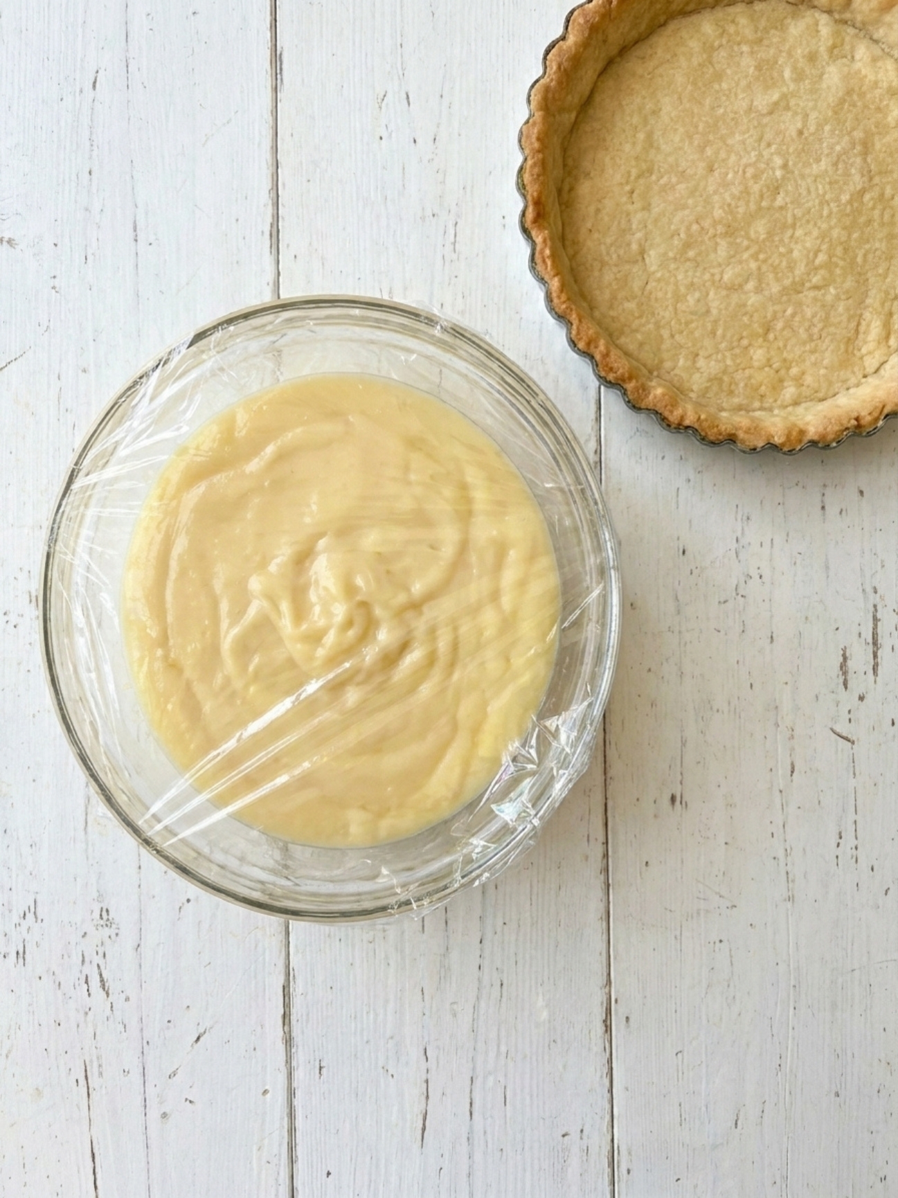 Crème pâtissière pour tarte aux fraises filmée au contact à côté d un fond de pâte cuit.