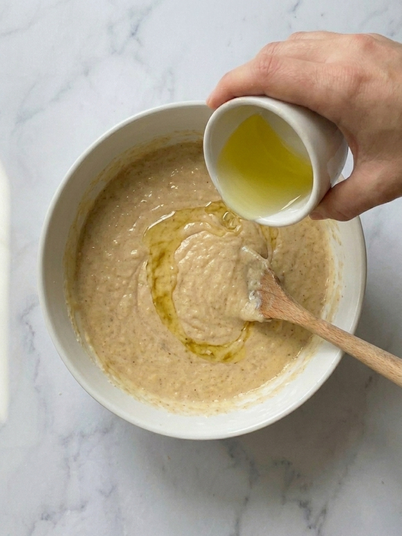 Verser de l'huile végétale dans une pâte lisse pour gateau yaourt banane.