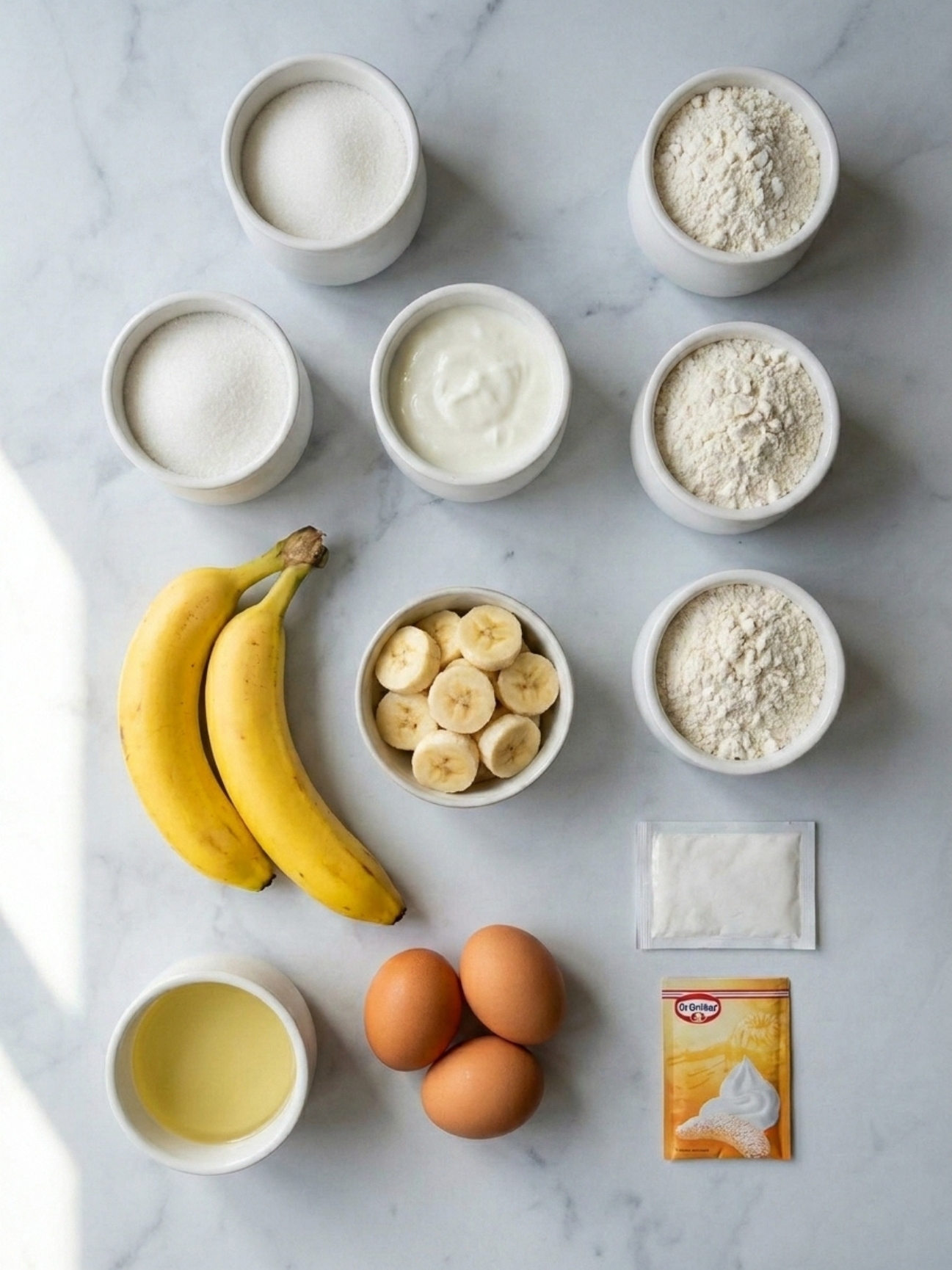 Ingrédients alignés sur marbre avec bananes et yaourt pour faire un gateau yaourt banane.