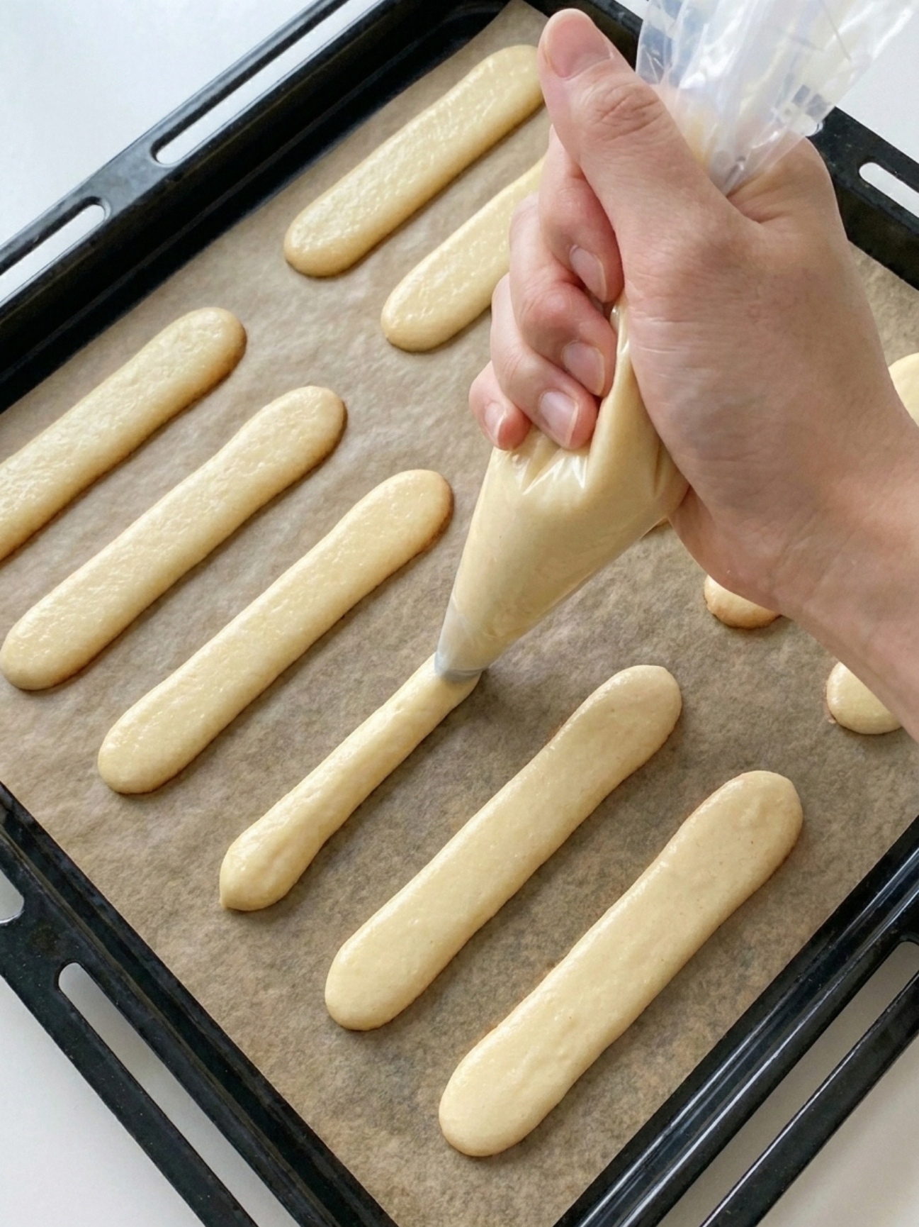Pochage de la pâte pour langue de chat recette facile sur une plaque de cuisson avec du papier sulfurisé.