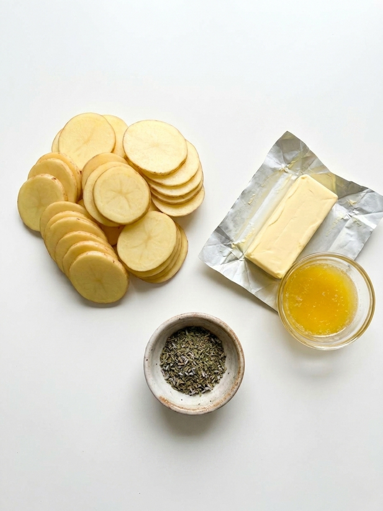 Ingrédients bruts, rondelles, beurre et herbes pour le mille feuille pomme de terre.
