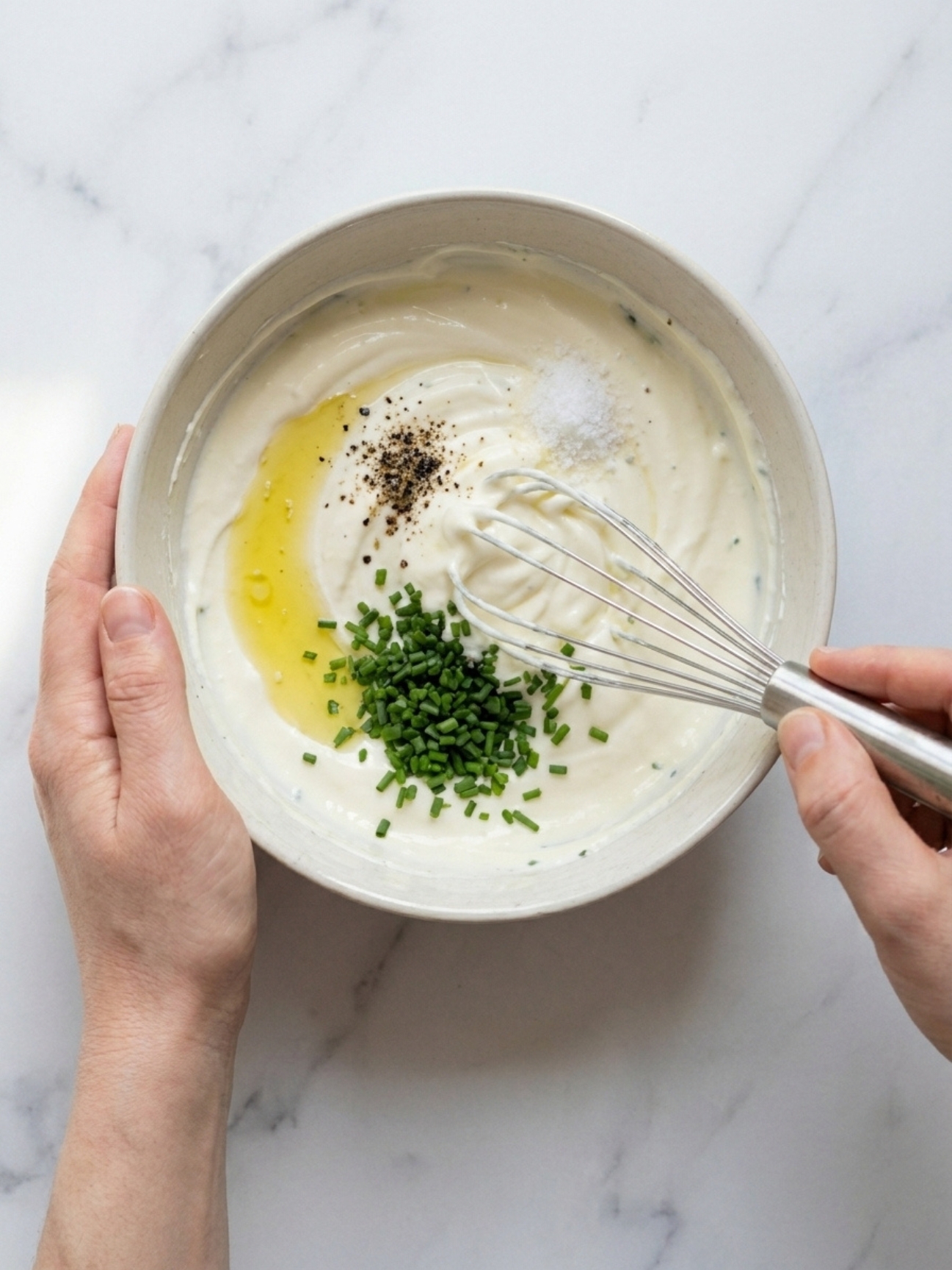 Une personne fouettant de la crème avec de la ciboulette et de l'huile dans un bol blanc pour la recette de mille feuille saumon.