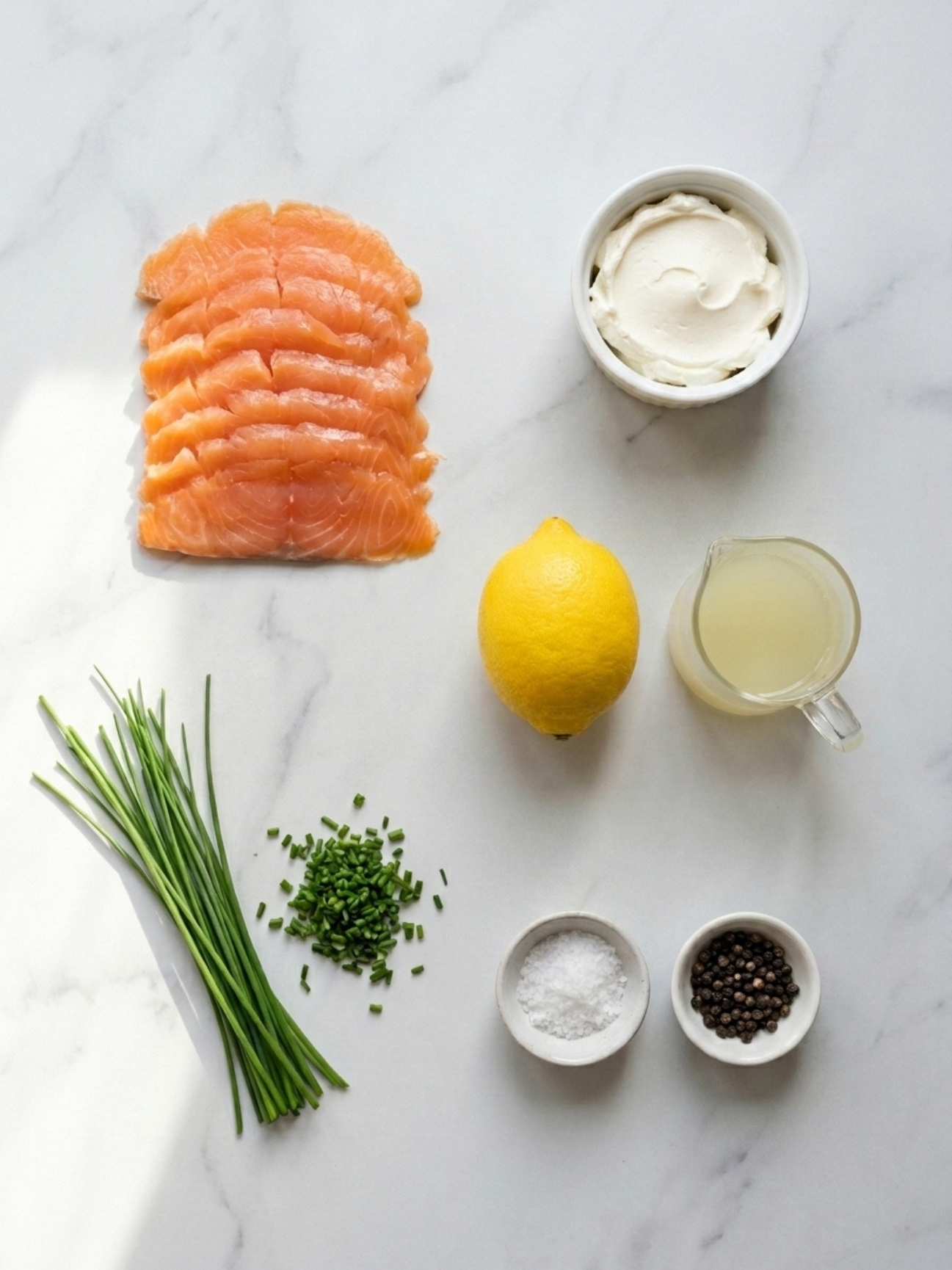 Ingrédients disposés à plat comprenant du saumon fumé, du fromage à la crème, un citron et de la ciboulette pour faire un mille feuille saumon.