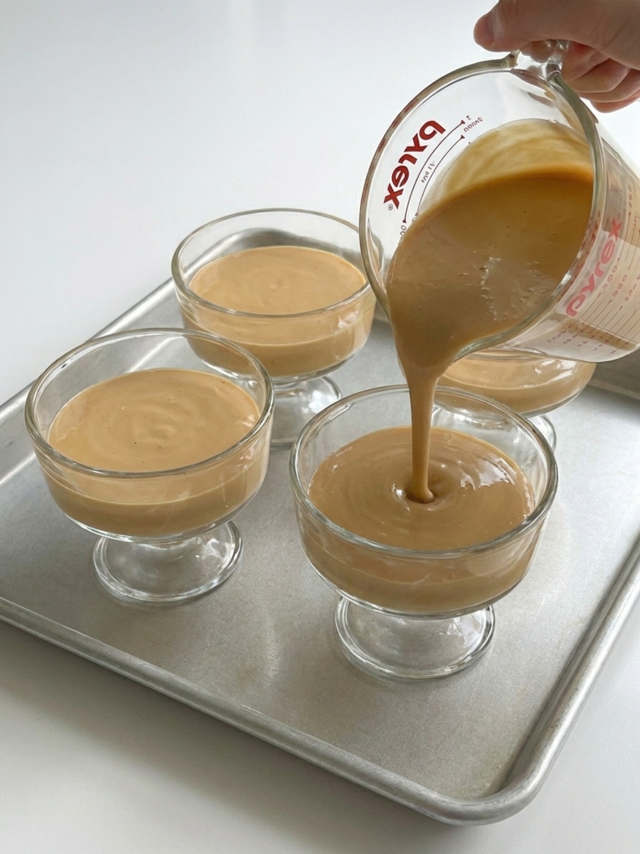 Une crème au caramel est versée depuis un pichet doseur dans des coupes, recette avec gélatine en feuille.