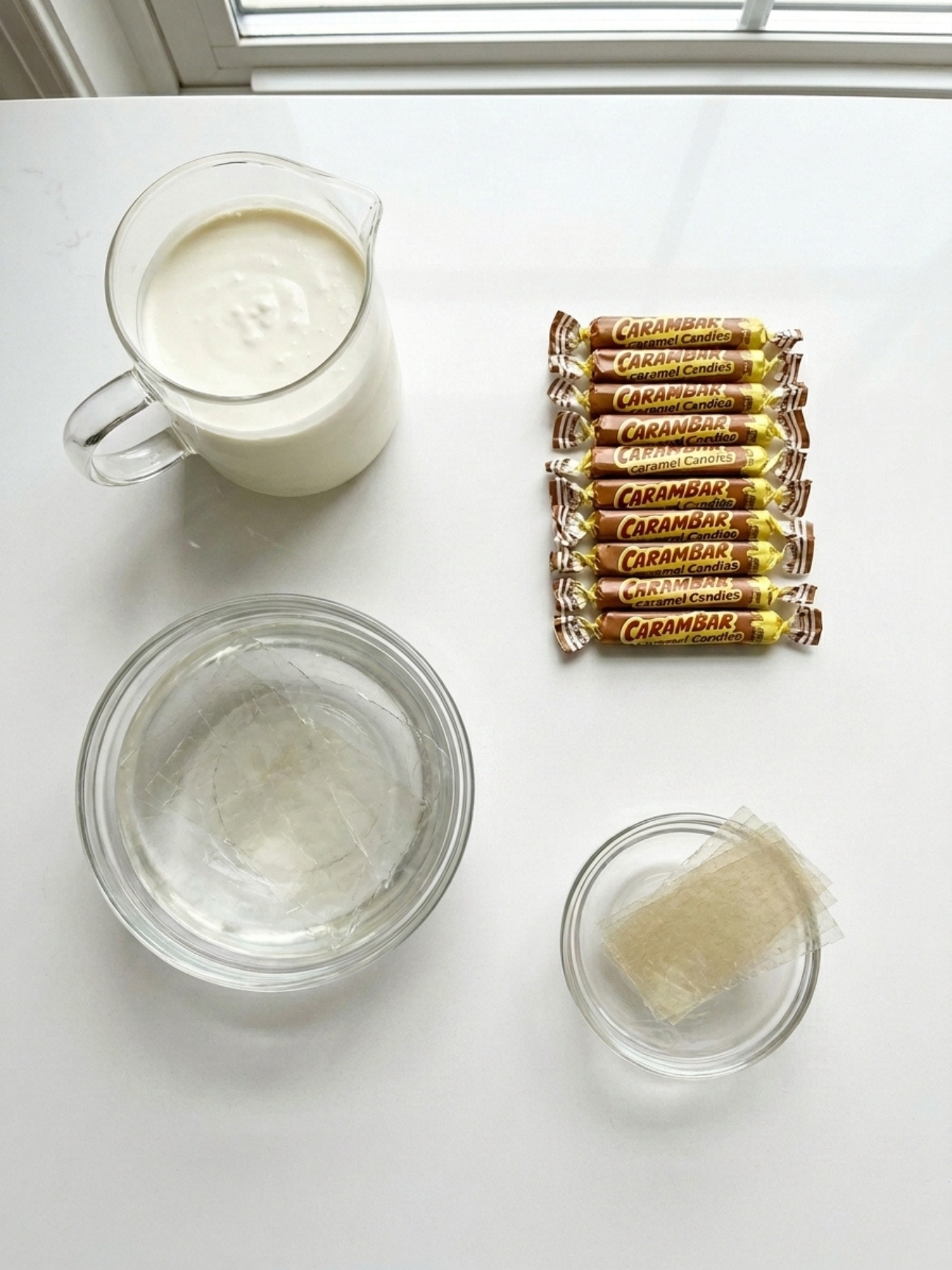 Crème, bonbons emballés, eau et feuilles transparentes sur fond blanc, recette avec gélatine en feuille.