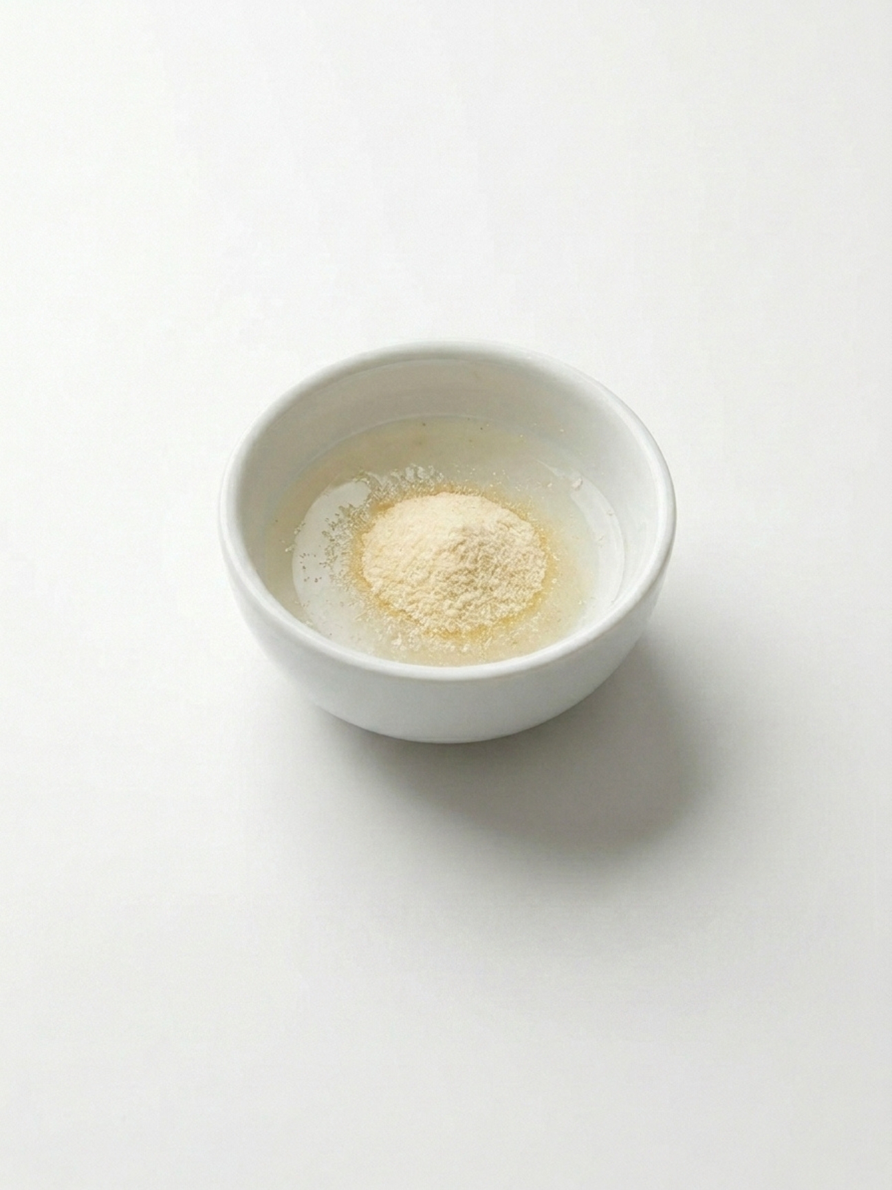 Poudre de gélatine s'hydratant dans un petit bol blanc pour la recette chantilly gelatine.