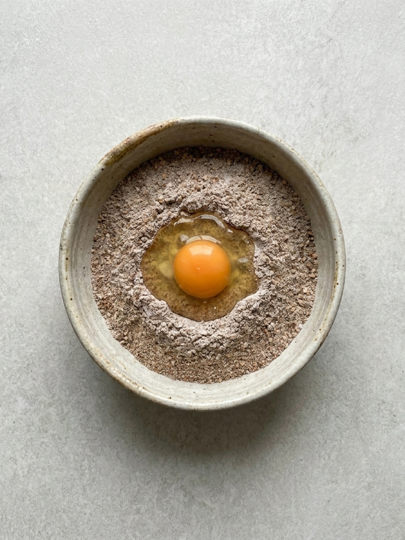 Puits de farine de blé noir avec un œuf au centre pour recette des galettes bretonnes au sarrasin.