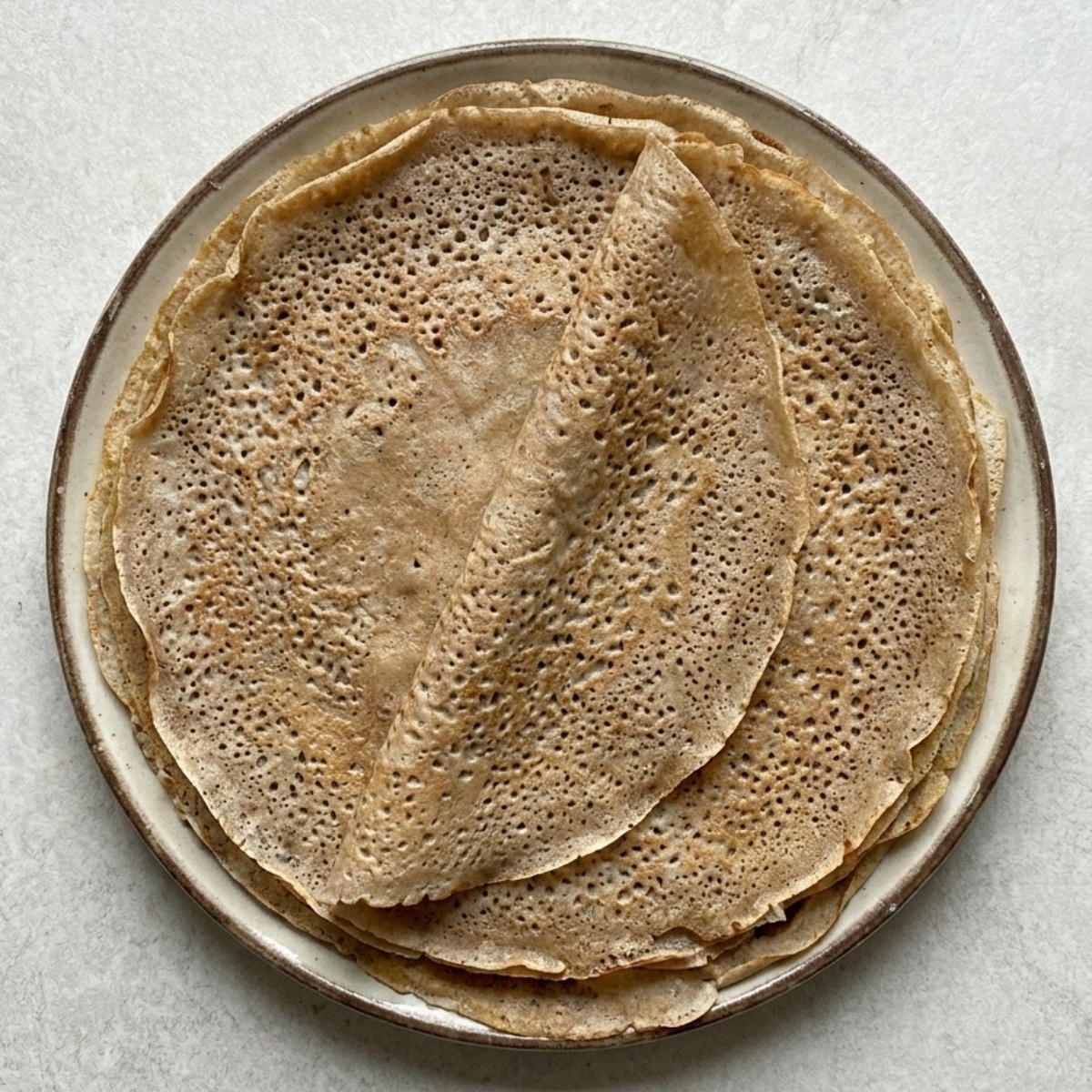 Pile de crêpes de blé noir dentelées prêtes pour la recette des galettes bretonnes au sarrasin.