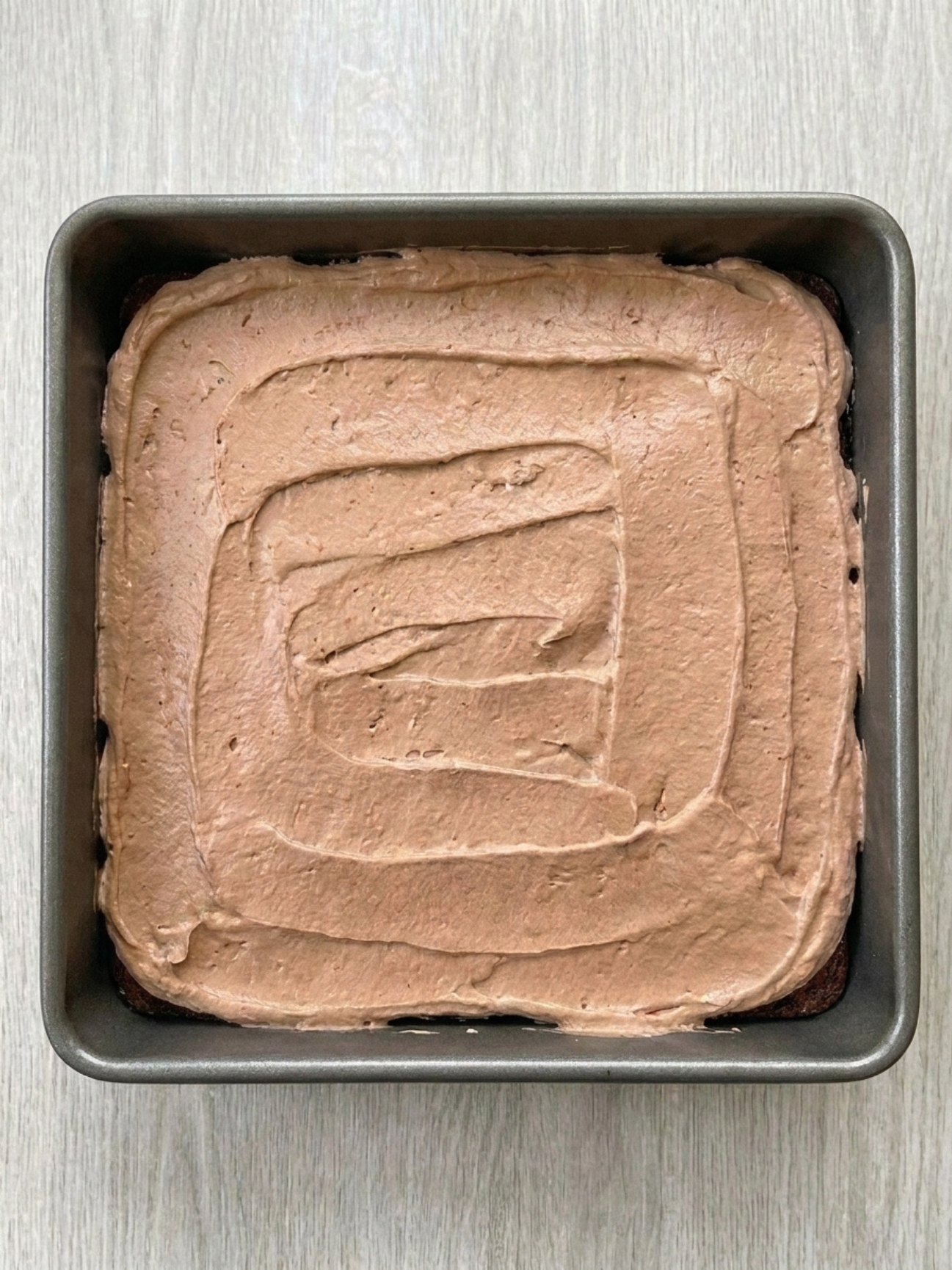 Crème au chocolat étalée uniformément dans un moule carré pour la recette gateau au kinder bueno.