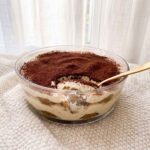 Tiramisu sans blanc d’œuf crémeux dans un plat rond, avec couches de biscuits au café, mascarpone et cacao.