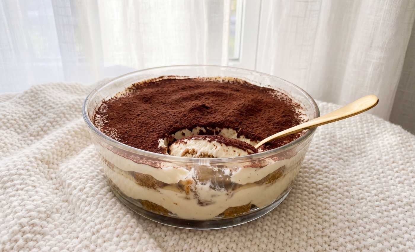 Tiramisu sans blanc d’œuf dans un plat en verre, garni de cacao et servi à la cuillère.